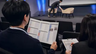 Asistentes revisan un programa de evento mientras se prepara una conversación en el escenario.