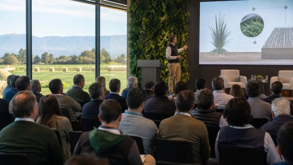 Asistentes siguen una conferencia técnica sobre producción de forrajes frente a un paisaje agrícola.