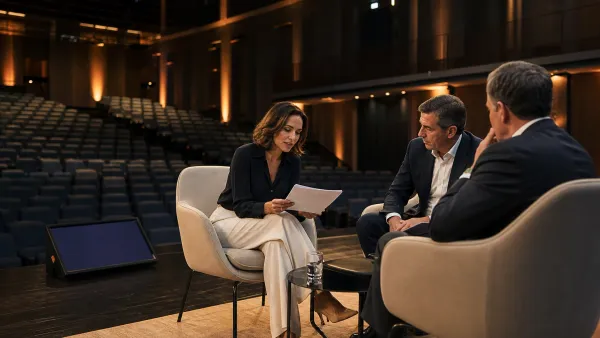 Moderadora revisando preguntas con dos invitados antes de una conversación en un auditorio corporativo vacío.