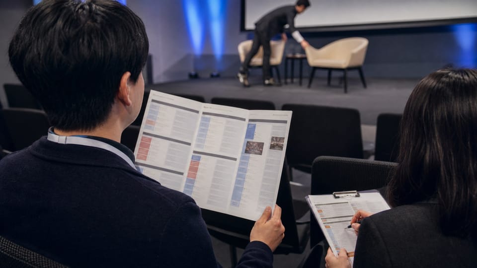 Asistentes revisan un programa de evento mientras se prepara una conversación en el escenario.